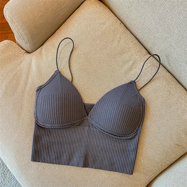 The Womens Sexy Halter Crop Top, featuring ribbed fabric and European styling in dark gray, with thin straps, is displayed flat on a light beige upholstered sofa.