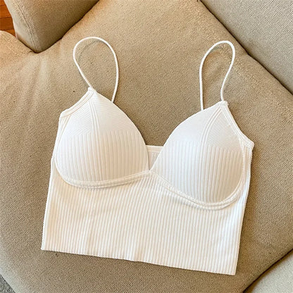 The Womens Sexy Halter Crop Top, in white with ribbed fabric and thin straps, is laid flat on a beige upholstered couch. It features European styling with subtle vertical stripes and lightly padded cups for a chic, comfortable look.