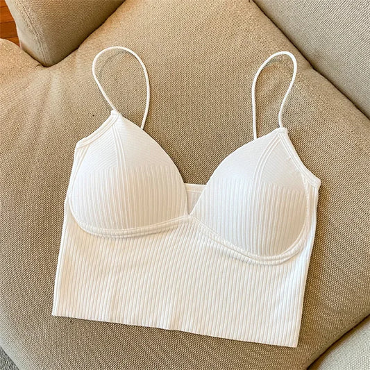 The Womens Sexy Halter Crop Top, in white with ribbed fabric and thin straps, is laid flat on a beige upholstered couch. It features European styling with subtle vertical stripes and lightly padded cups for a chic, comfortable look.